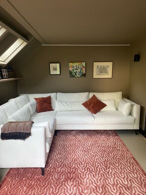 A white L-shaped sectional sofa with brown pillows, a patterned rug, and three framed artworks on the wall. - Beautiful villa with sauna, 10 min from the beach (Bentveld)