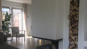 A modern living room with a fireplace, a dining area with a table and chairs, and a view through a sliding glass door. - Beautiful villa with sauna, 10 min from the beach (Bentveld)