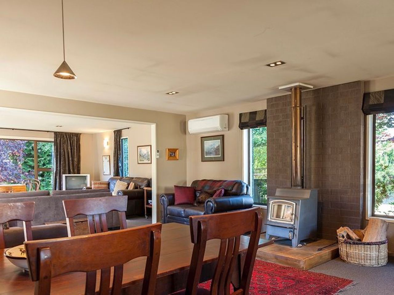 A cozy living room with a fireplace, a dining area with wooden furniture, and a large window offering a view of the outdoors.