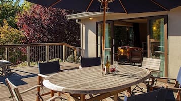 A wooden deck with a round table and chairs, an umbrella, and a bar area with a glass enclosure.