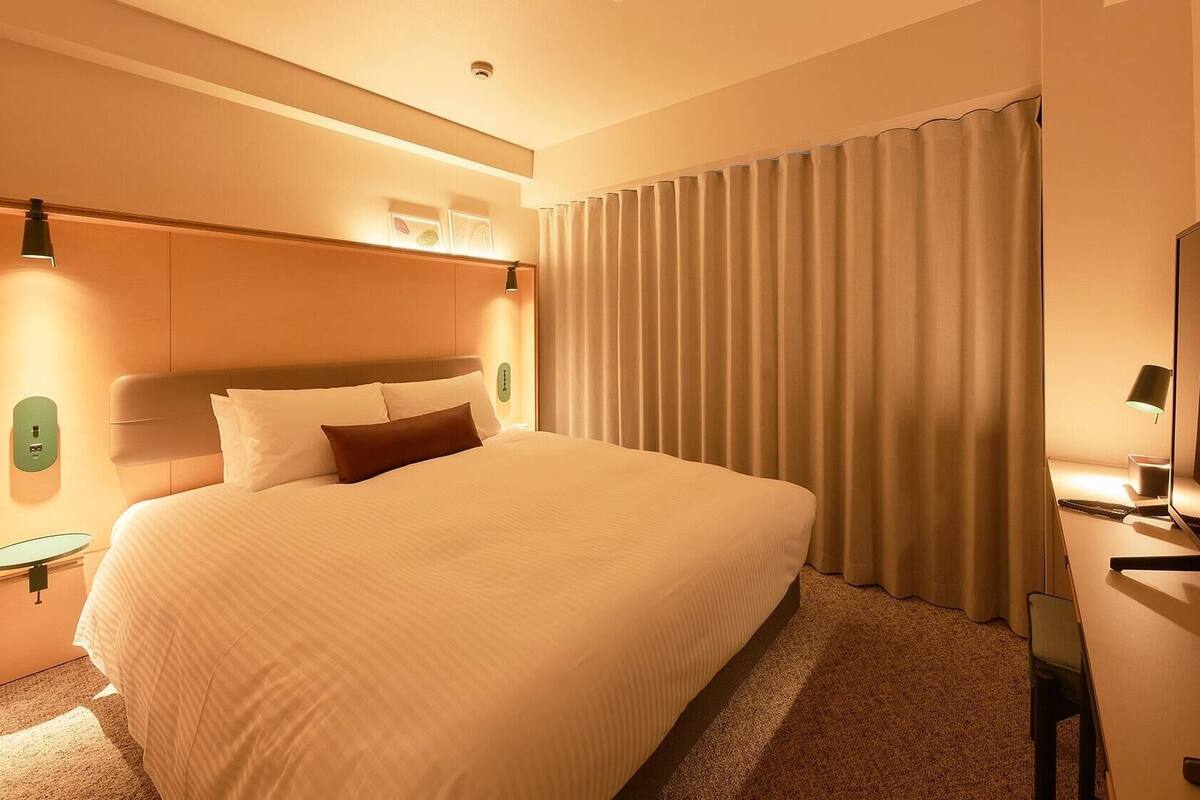 A hotel room with a large bed, a desk with a flat-screen TV, and a window with curtains.