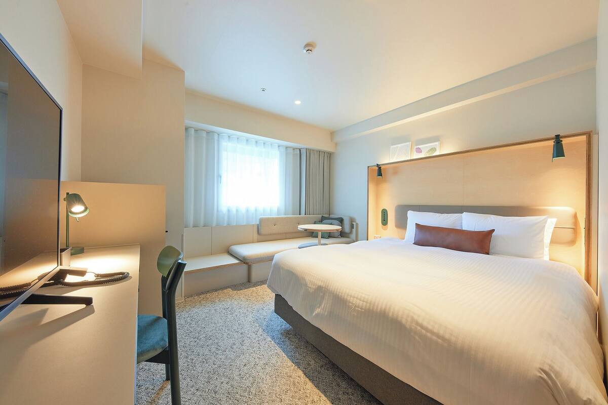 A hotel room with a large bed, a seating area with a table, and a desk with a lamp.