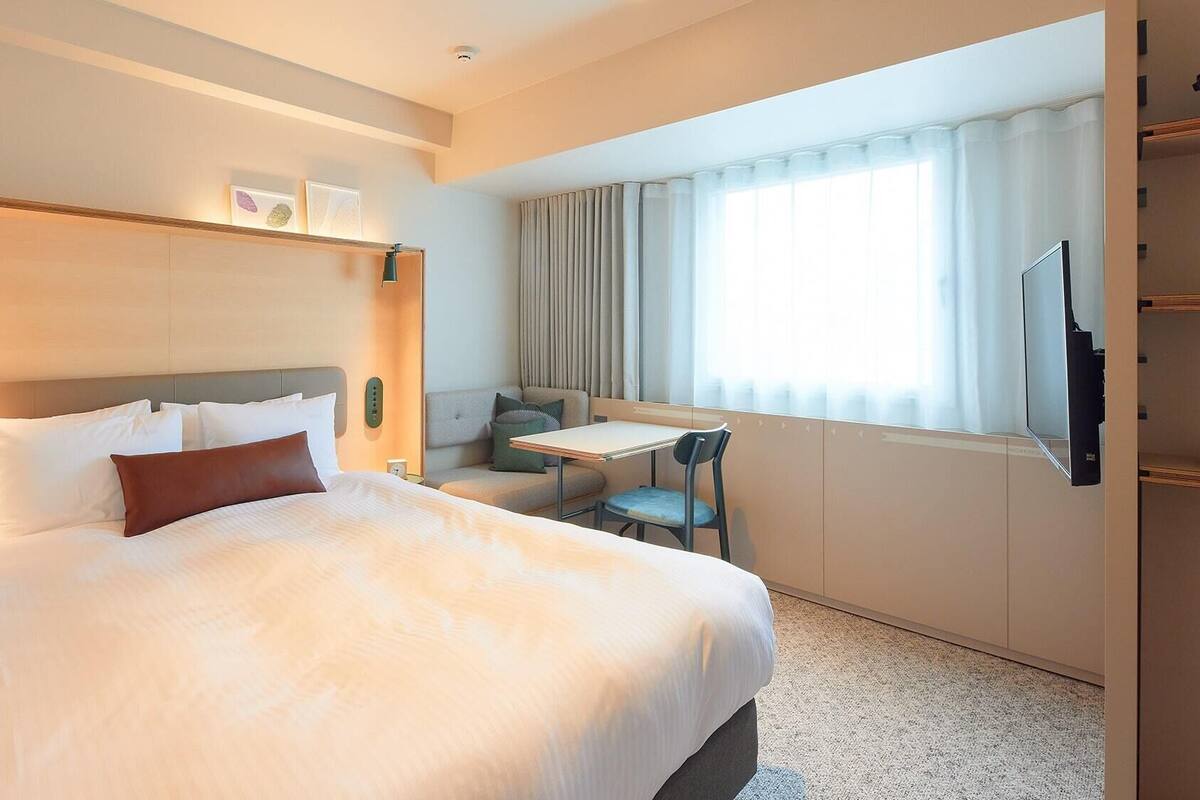 A hotel room with a bed, a desk, a chair, and a window with curtains.