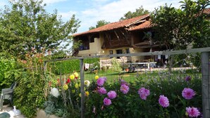 A rustic wooden house with a tiled roof, surrounded by a garden with various flowers and a wooden fence. - Gîtes Pyrénées Les Trois Montagnes BALOU (Ganties)