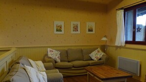 A living room with a sofa, a wooden coffee table, and a radiator. There are three framed pictures on the wall. - Gîtes Pyrénées Les Trois Montagnes BALOU (Ganties)
