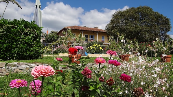 A garden with various flowers and a building with a tiled roof.
