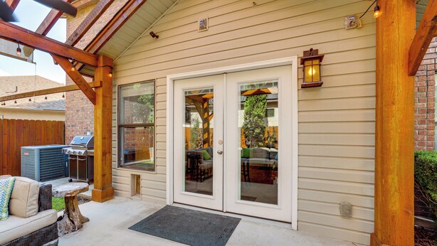 A covered patio with a grill, outdoor seating, and a wooden pergola.