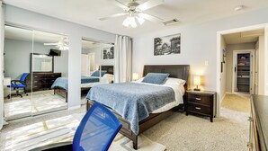 A bedroom with a bed, a desk, a chair, a nightstand, a lamp, a ceiling fan, and a closet.