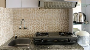 A kitchen with a gas stove, a sink, a stainless steel range hood, and a tiled backsplash. - Homey And Cozy Stay 2Br At Green Pramuka City Apartment (Jakarta)