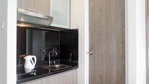 A modern kitchen with a black countertop, stainless steel sink, and a white kettle. - Exclusive And Comfy Studio Room Apartment At Taman Melati Surabaya (Surabaya)