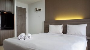 A hotel room with a large bed, a flat-screen TV, and a wooden wardrobe. - Cozy And Compact Studio Apartment At Taman Melati Surabaya (Surabaya)