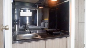 A compact kitchen with a stainless steel sink, a black induction cooktop, and a Modena range hood. - Cozy And Compact Studio Apartment At Taman Melati Surabaya (Surabaya)
