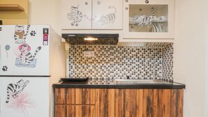 A kitchen with wooden cabinets, a black countertop, a stainless steel sink, and a refrigerator with cat-themed magnets. - Comfort 1Br With Working Room At Meikarta Apartment (Cikarang)