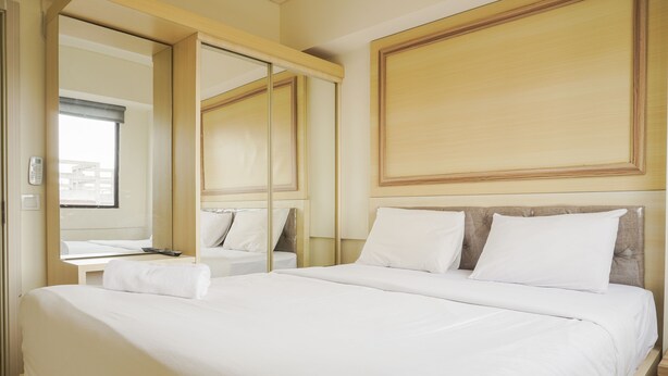 A hotel room with a large bed, a bedside table, a mirror, and a window. - Comfort 1Br With Working Room At Meikarta Apartment (Cikarang)