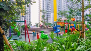 A playground with slides and climbing structures surrounded by greenery and tall buildings. - Fancy And Nice Studio Apartment At Springlake Summarecon Bekasi (Bekasi)