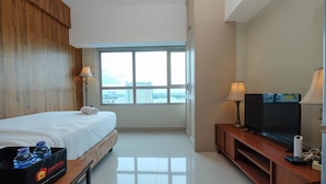 Ein Hotelzimmer mit einem Bett, einem Fernseher auf einer Holzkonsole, einem Fenster mit Blick auf die Stadt und einem Serviertisch mit Wasserflaschen.