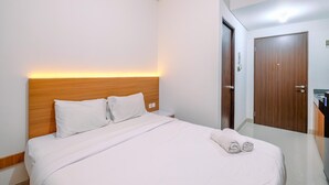 Una camera d'albergo con una testiera in legno, un letto rifatto con lenzuola bianche e un paio di asciugamani arrotolati sul letto.
