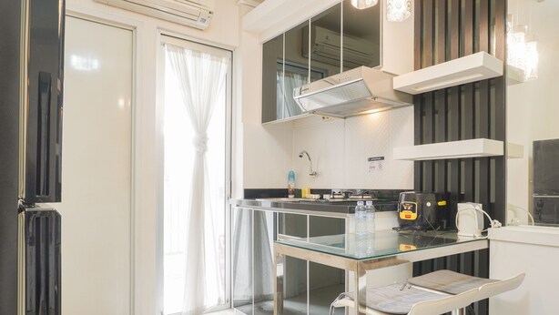 A modern kitchen with a glass-top table, a built-in oven, and a coffee machine. - Comfort Living And Minimalist 1Br At Bassura City Apartment (Jakarta)