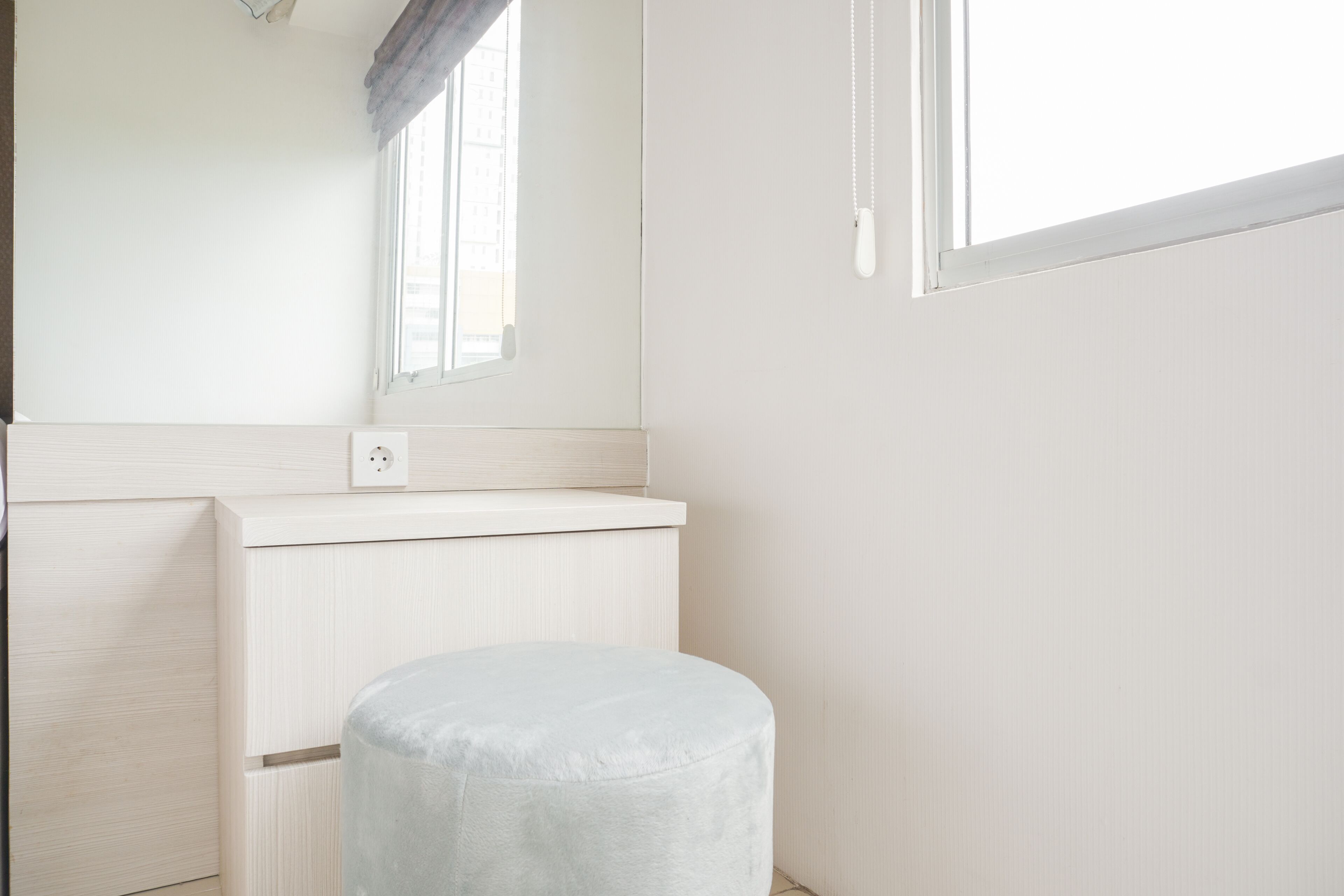 A minimalist bathroom with a round stool, a mirror, and a window.