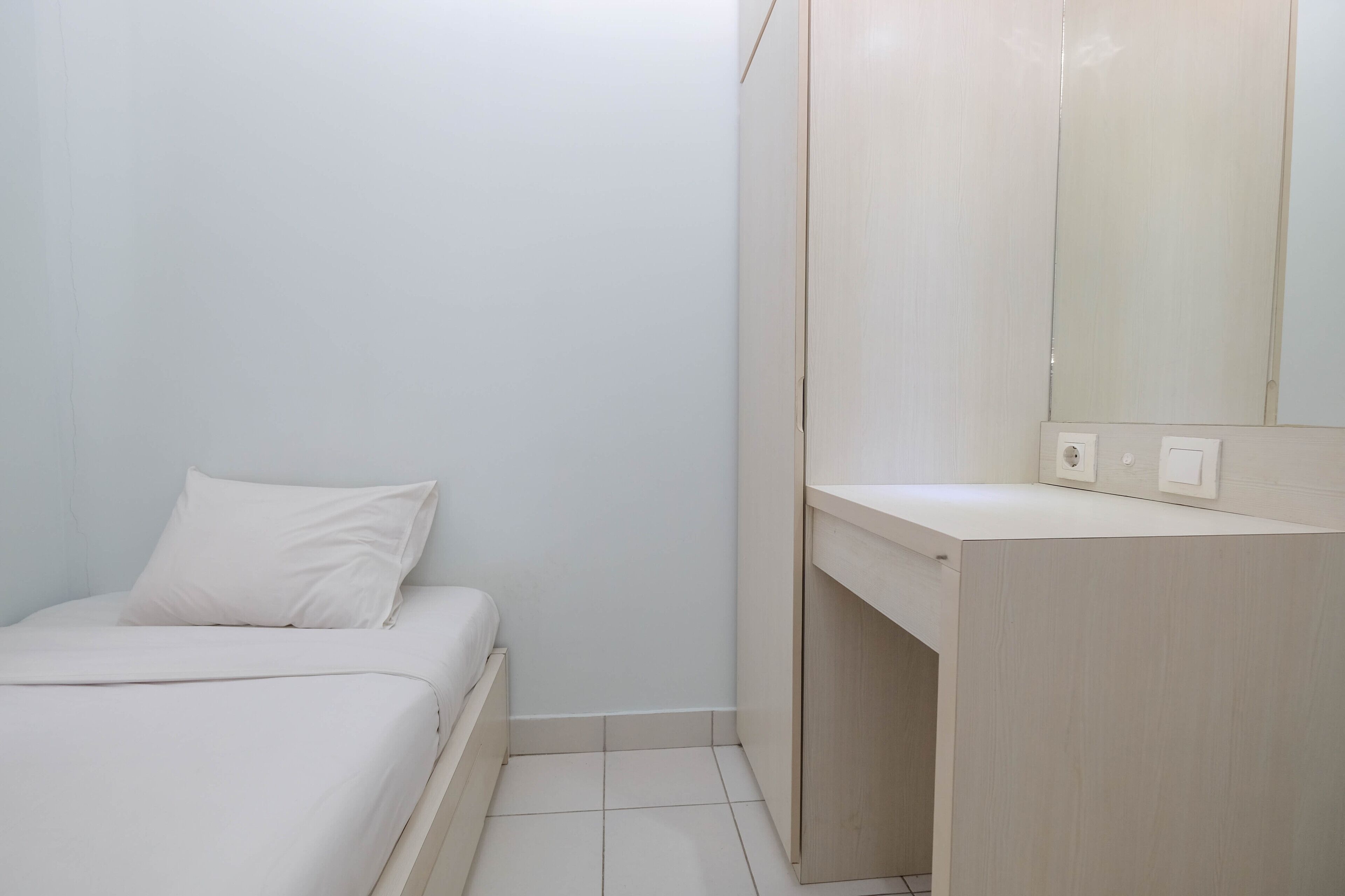 Une petite pièce propre, avec un lit, une commode en bois et un miroir.