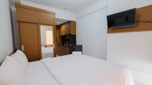 A hotel room with a large bed, wooden wardrobe, kitchenette, and a mounted TV. - Comfort Studio Apartment At Patraland Urbano (Bekasi)