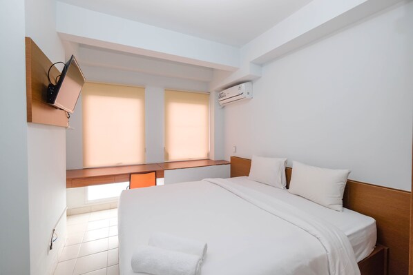 A hotel room with a bed, a desk, an air conditioner, and a TV mounted on the wall. - Luxurious Studio At Patraland Urbano Apartment (Bekasi)