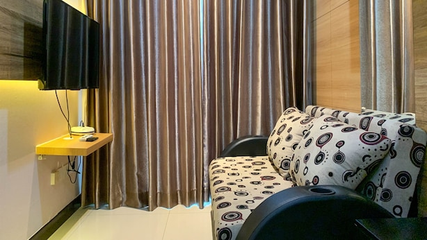 Un salon moderne avec un téléviseur à écran plat fixé au mur, un canapé agrémenté de coussins à motifs et une grande fenêtre avec des rideaux.
