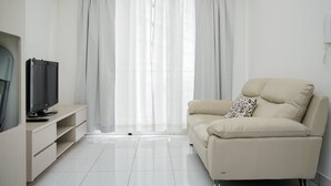 A modern living room with a beige sofa, a flat-screen TV, and a white entertainment unit. - Modern Look And Comfy 2Br At Casa De Parco Apartment (Pagedangan)
