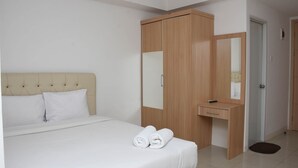 A hotel room with a bed, a wooden wardrobe, a small desk, and a mirror. - Cozy And Strategic Studio At Bassura City Apartment (Jakarta)