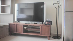 A flat-screen TV on a wooden TV stand with a remote control, a small speaker, and a water bottle. - Warm And Cozy Studio At Springlake Summarecon Apartment (Bekasi)