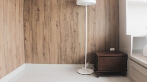 A corner of a room with a wooden wall, a white floor lamp, and a small wooden nightstand. - Warm And Cozy Studio At Springlake Summarecon Apartment (Bekasi)