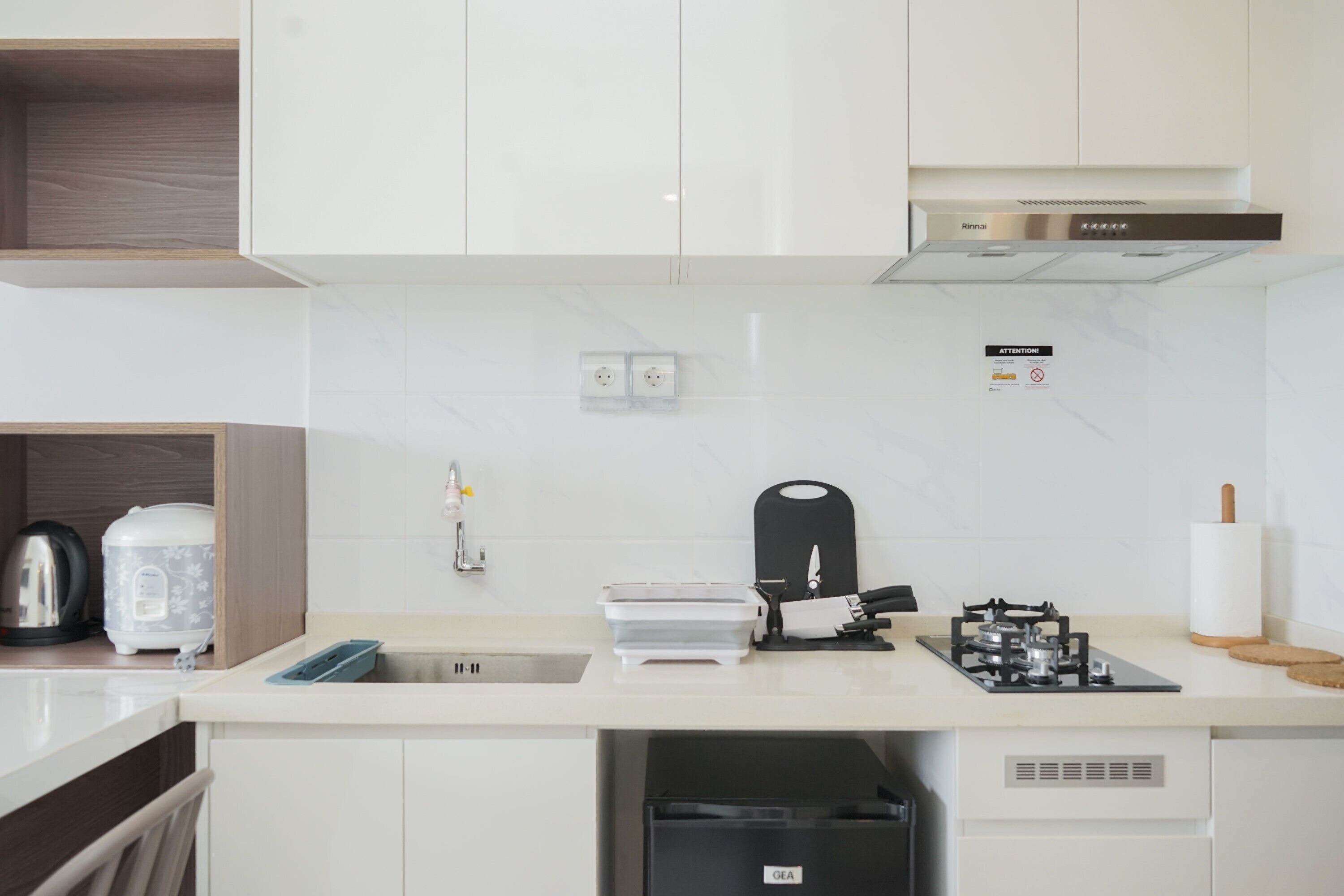 A modern kitchen with white cabinets, a stainless steel range hood, a built-in dishwasher, and a countertop with a kettle, toaster, and other appliances.