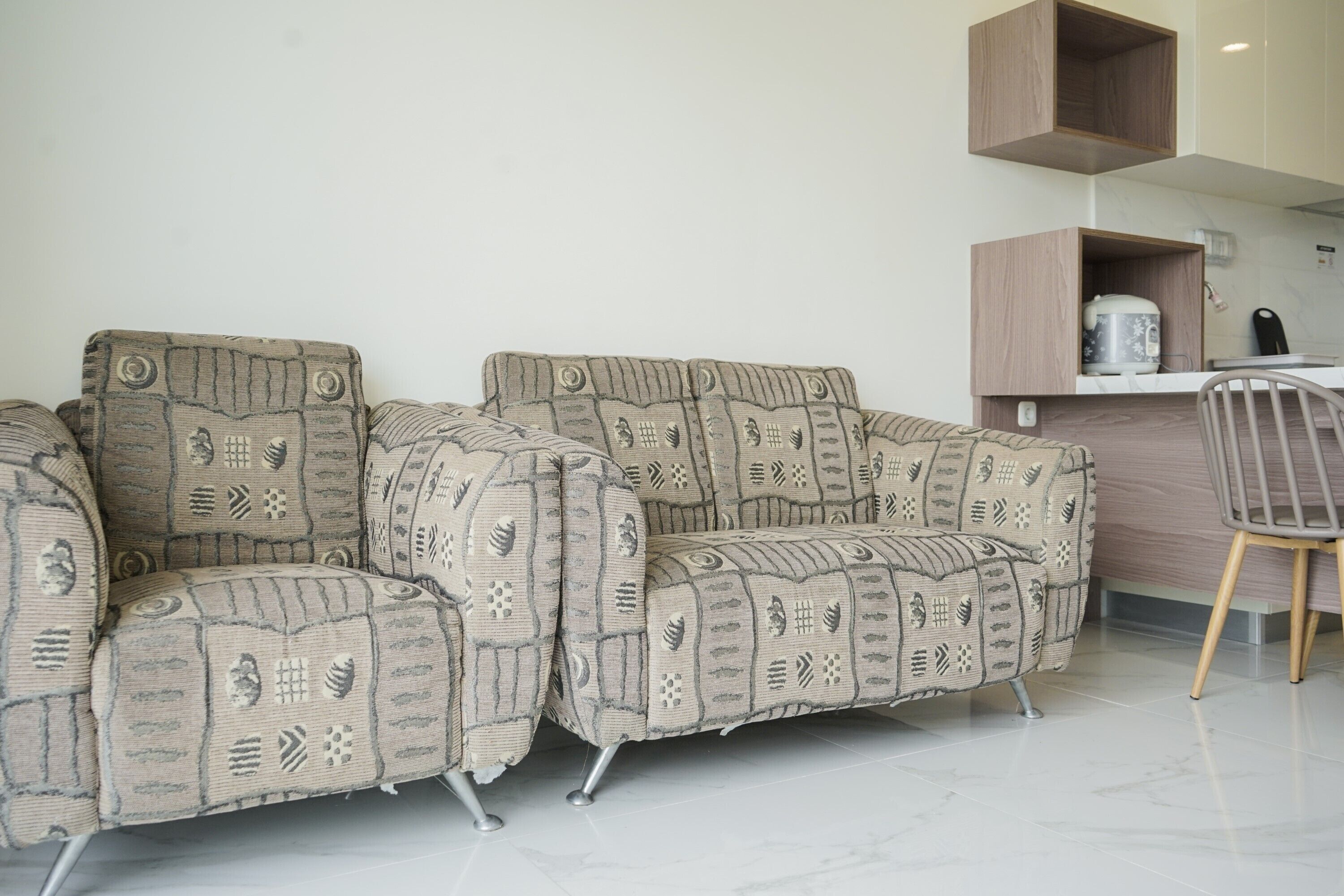 A sofa with a patterned fabric, a wooden cabinet above it, and a chair to the right.