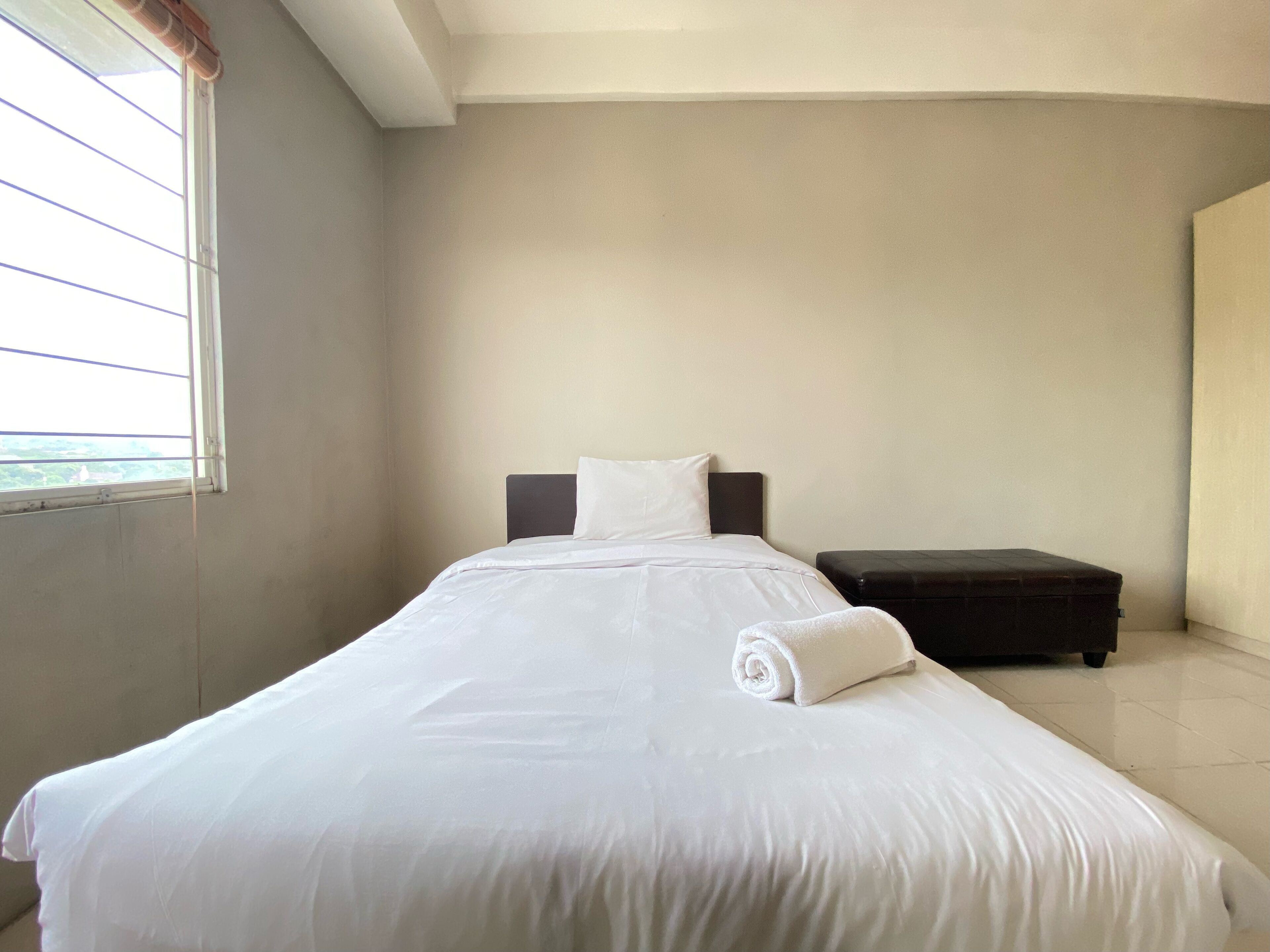 A neatly made bed with white linens, a dark headboard, and a rolled towel on the footboard.