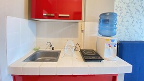 Et køkken med et rødt skab, en vask, en vanddispenser og en elkedel.