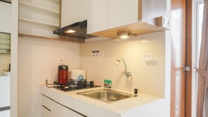 A compact kitchen with a stainless steel sink, a built-in range hood, and a small countertop with a kettle and a coffee maker.