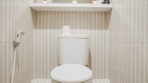 A white toilet with a tank, a showerhead, and a wall-mounted shelf with small plants.