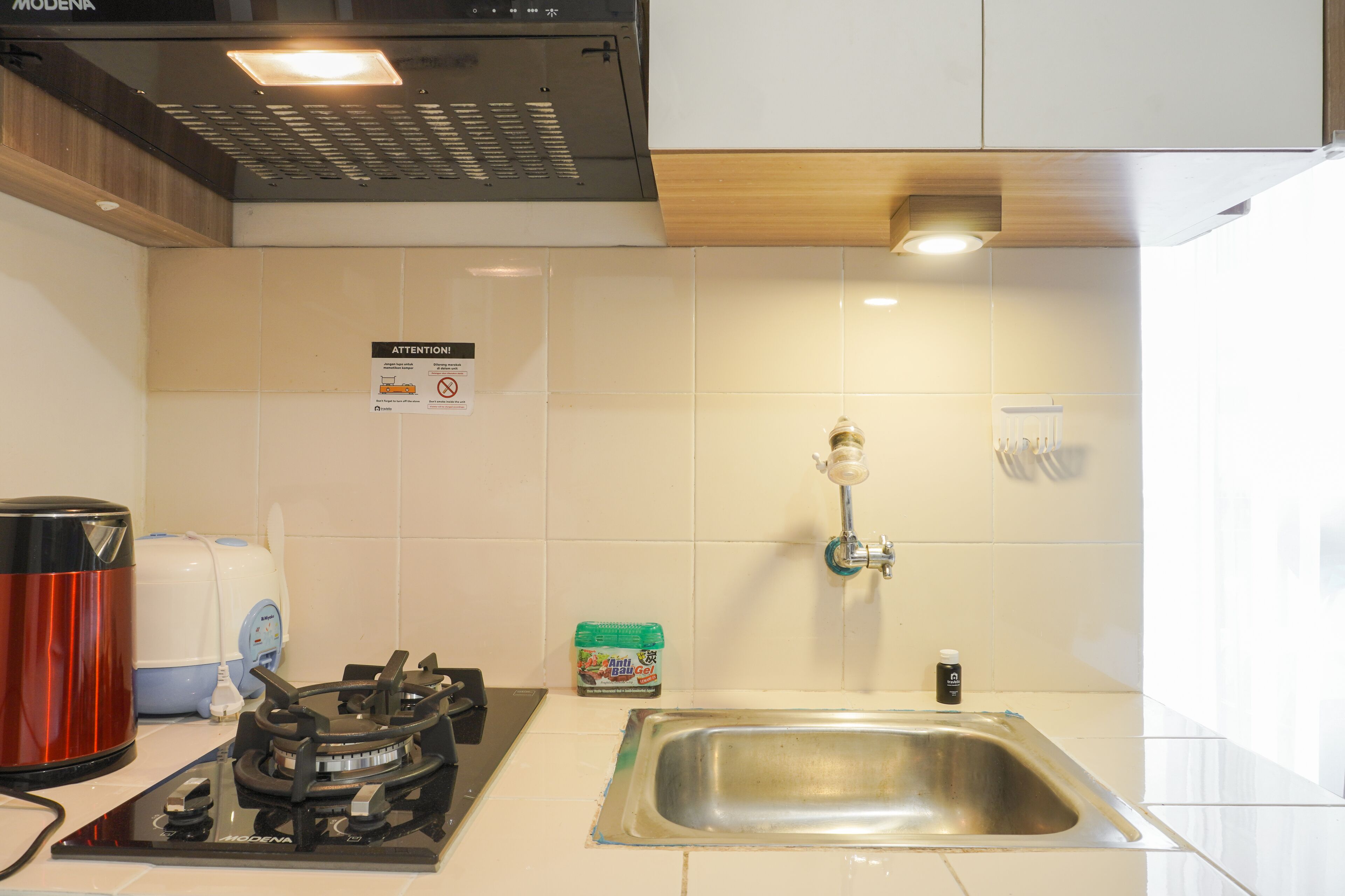 Una cocina con estufa a gas, lavamanos, cafetera y un letrero de precaución en la pared.
