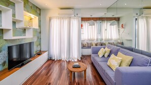 A modern living room with a flat-screen TV, a sofa with cushions, a coffee table, and a large mirror reflecting the room.
