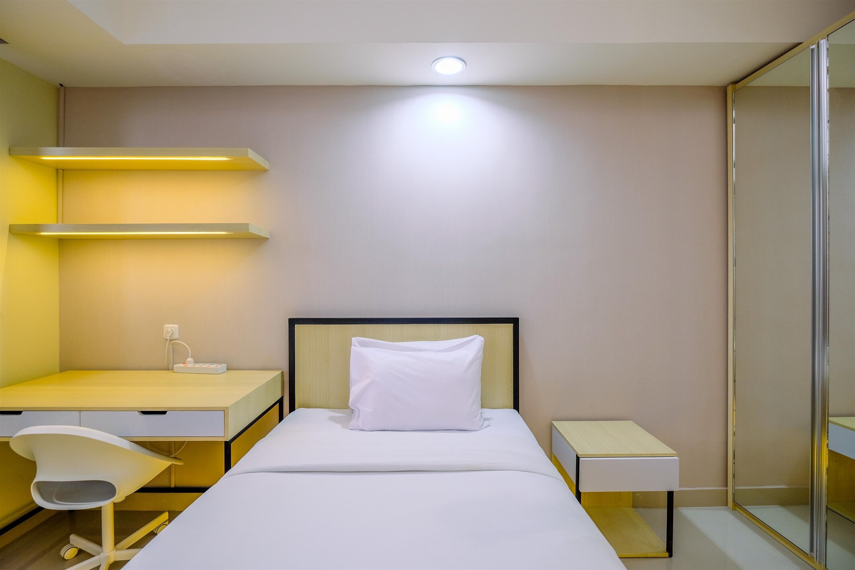 A hotel room with a bed, a desk, a chair, and a bedside table.