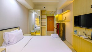 A hotel room with a bed, a TV, a minibar, and a bathroom visible through an open door. - Comfy And Minimalist Studio At Evenciio Margonda Apartment (Depok)