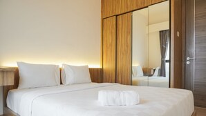 A neatly made bed with white linens and pillows, a wooden headboard, and a large mirror reflecting the room.