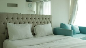 A neatly made bed with white linens and a tufted headboard. There is a teal sofa with matching cushions in the background.