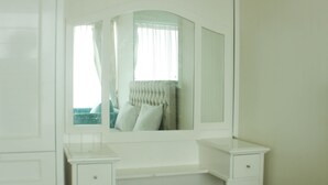 A white vanity with a mirror, a small stool, and a drawer.