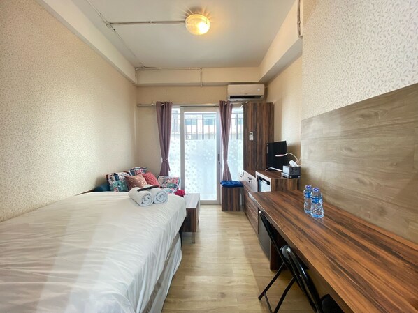 A hotel room with a bed, a desk, a TV, and a window with curtains.