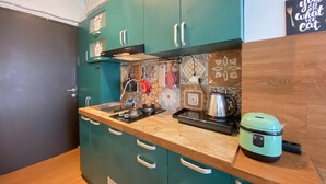 Cozinha compacta com armários verde-turquesa, bancada, fogão, chaleira e cozidela de arroz.