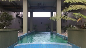 Piscina interior com bordas azuis em azulejos, rodeada por colunas e plantas em vasos.