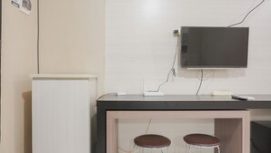 A small kitchenette with a refrigerator, a counter with a flat-screen TV, and two stools. - Comfort Studio At Kebagusan City Apartment (Jakarta)