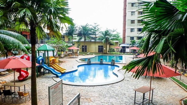 A children's play area with slides and a pool, surrounded by palm trees and outdoor seating. - Comfort Studio At Kebagusan City Apartment (Jakarta)