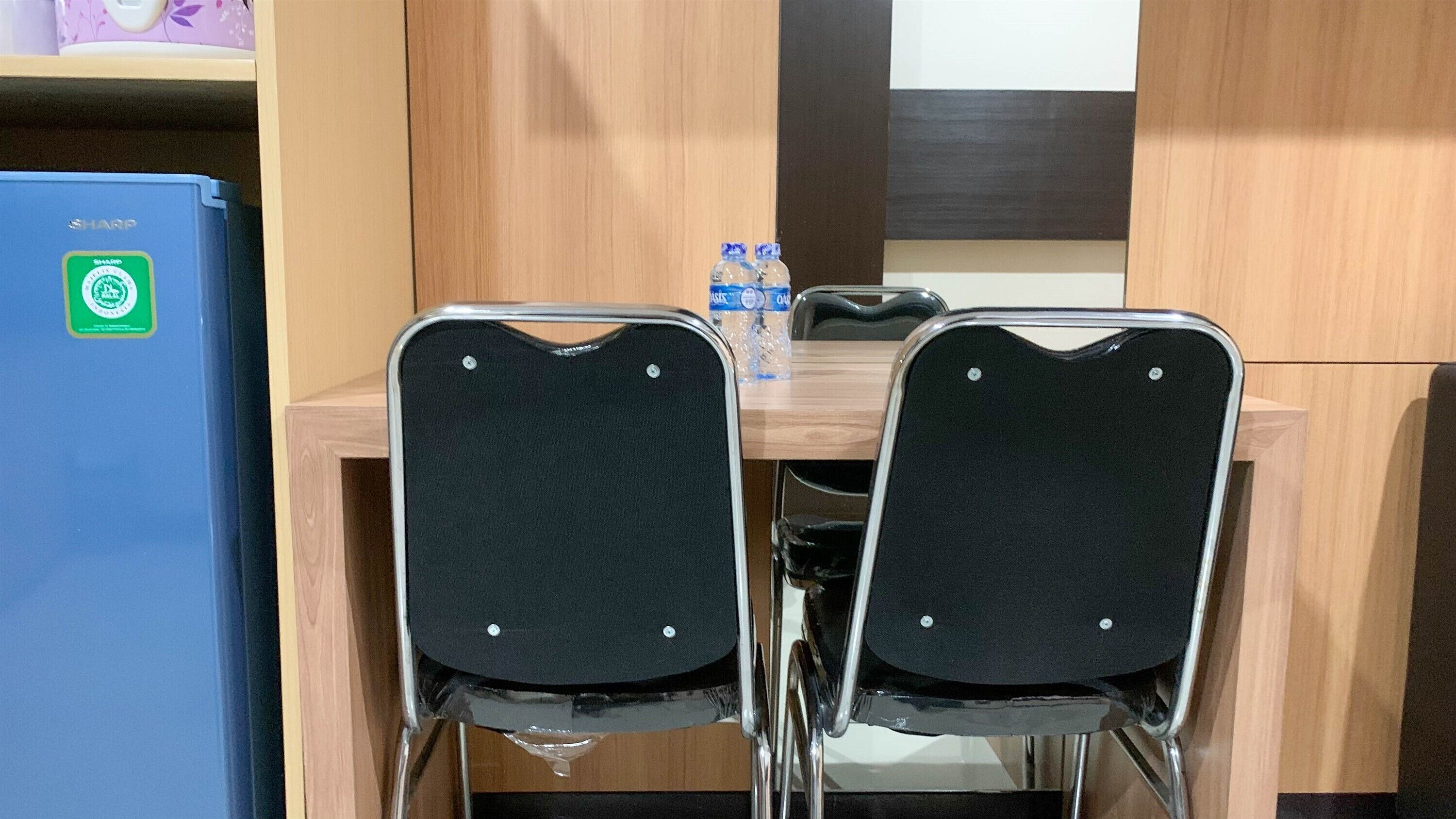 A room with two black chairs with chrome legs, a wooden table, and a blue refrigerator with a green sticker.